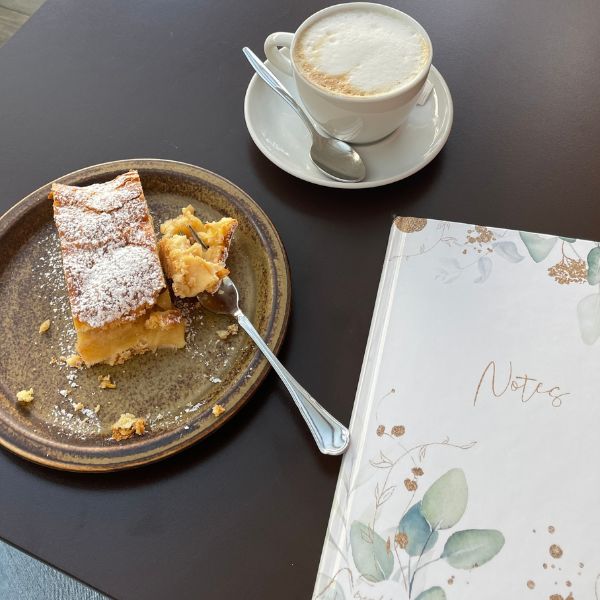 Blick auf einen Kaffeetisch, mit Kuchen, Kaffee und einem Notizbuch