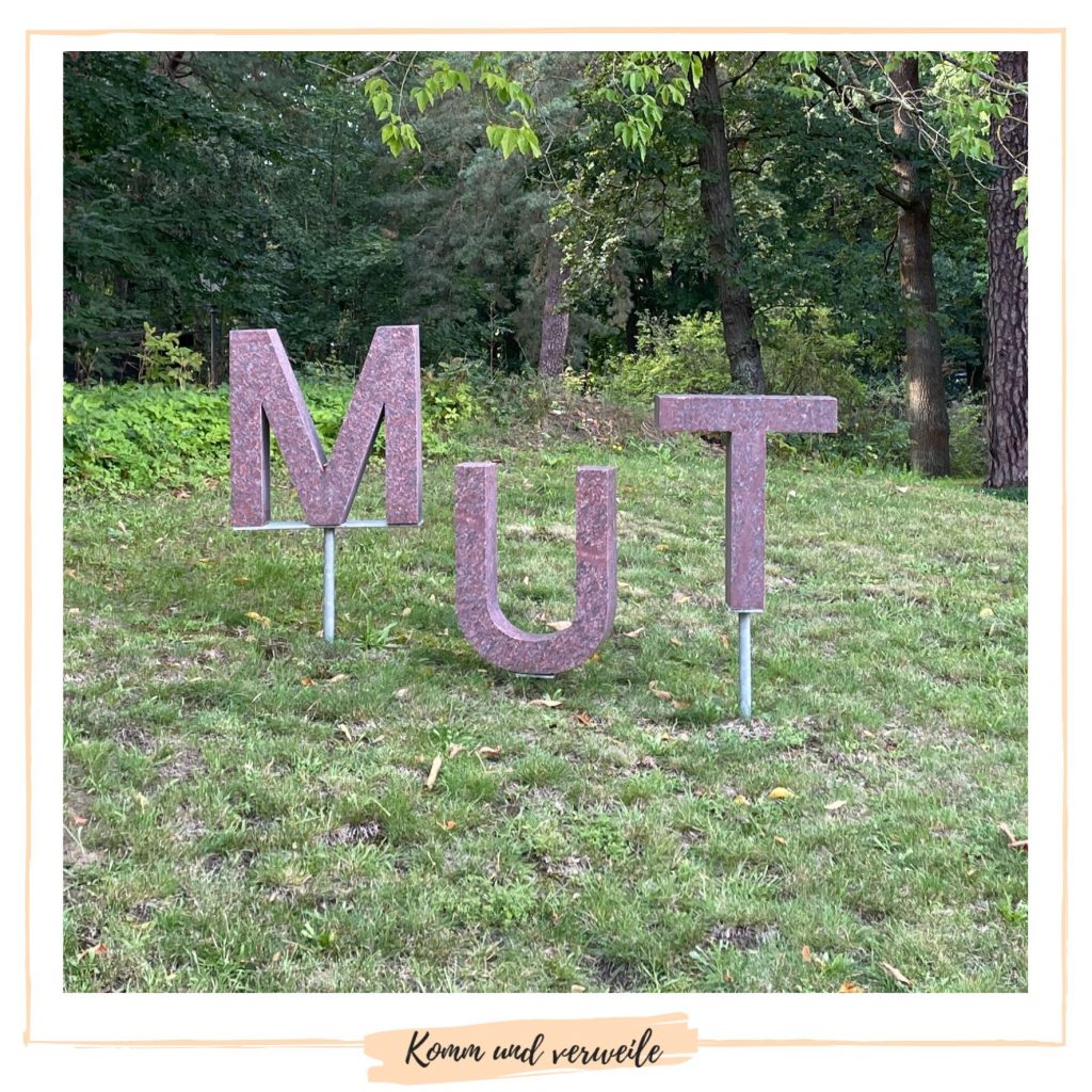 Eine Wiese auf der die das Wort MUT in Metallbuchstaben steht