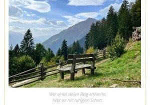 Holzbank mit Blick auf die Berge – Symbol für Innehalten und Reflexion, begleitet vom Zitat: "Wer einen steilen Berg erklimmt, hebt an mit ruhigem Schritt." – Komm und verweile